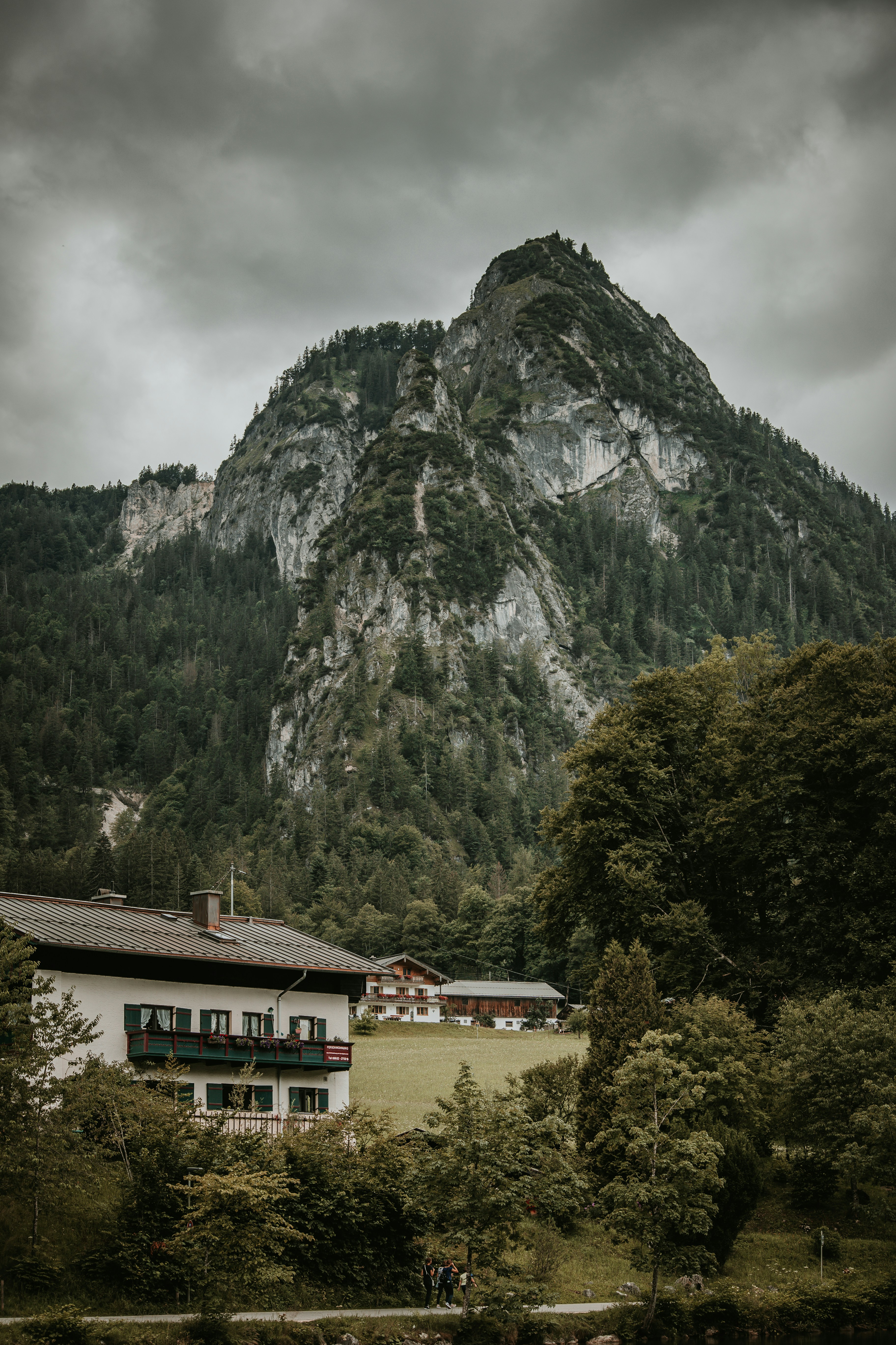 Rugged granite peak towers over a grassy valley and Alpine village, with dark storm clouds gathering above.