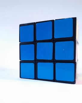 A partially solved Rubik's Cube with the visible side completely blue. The cube is placed against a light background, and the image captures it from an angle that highlights the orderly pattern.