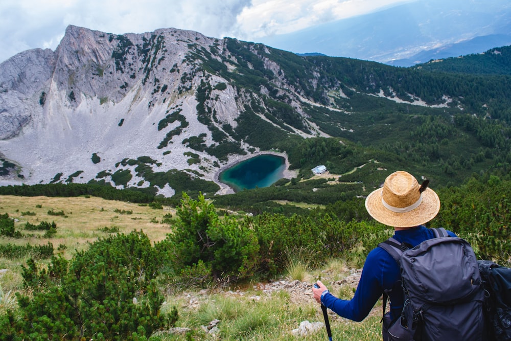 a person with a backpack and a hat is looking at a mountain lake