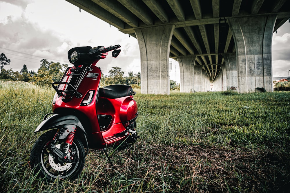 a red scooter parked in the grass under a bridge