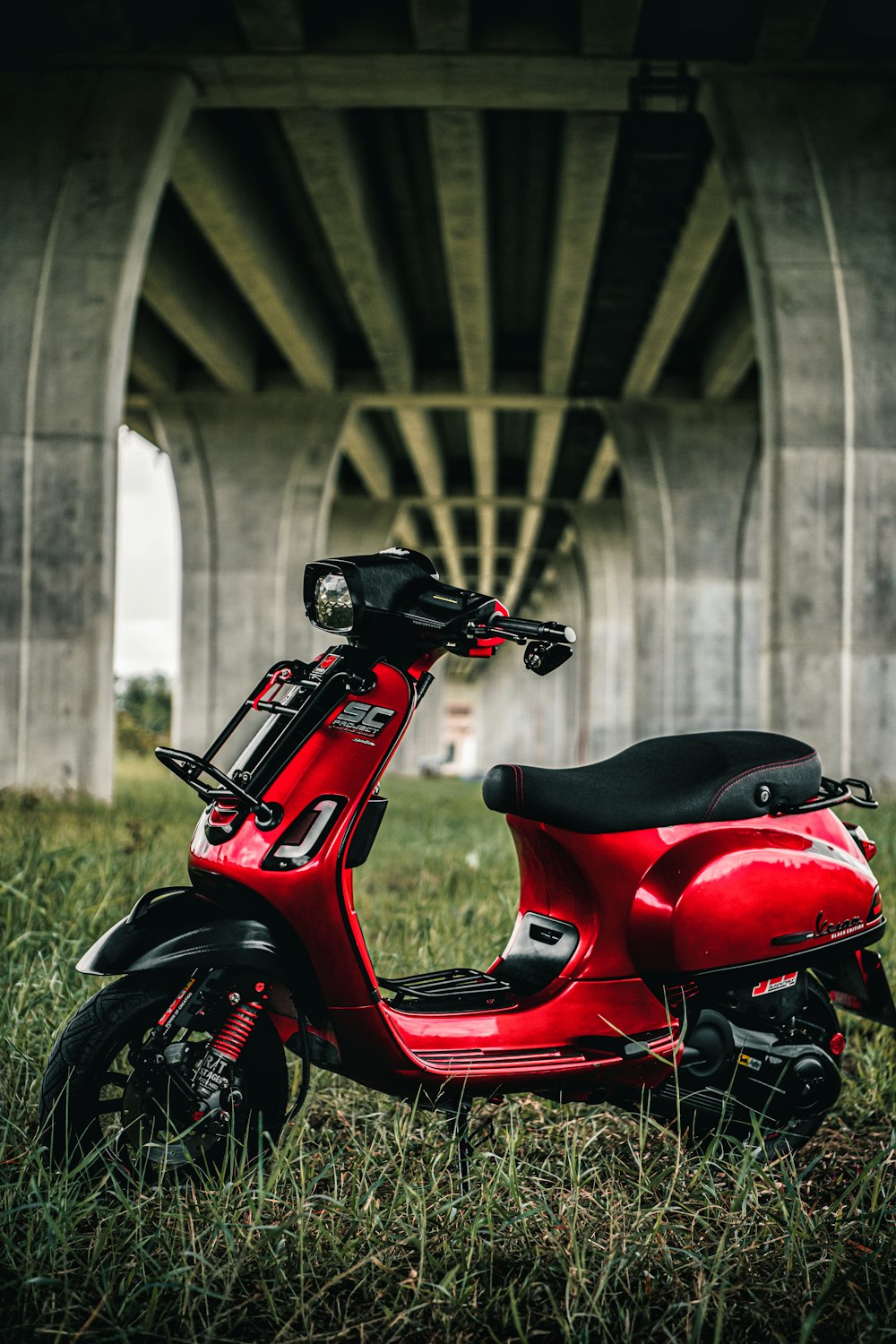 a red scooter parked in the grass under a bridge