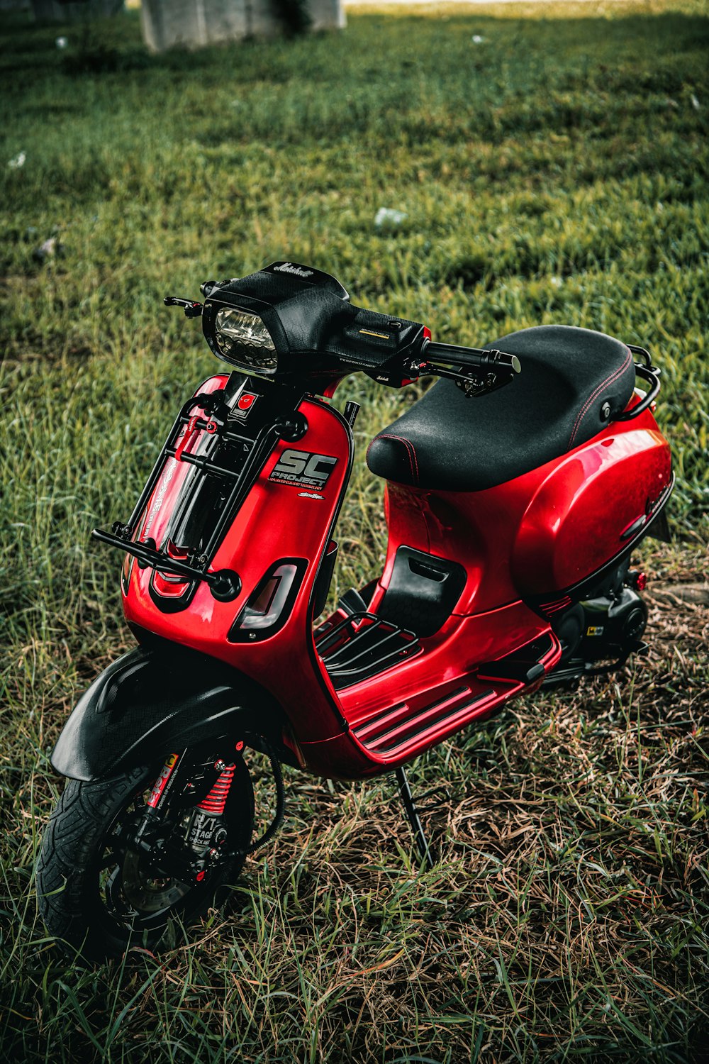 a red scooter is parked in a grassy field