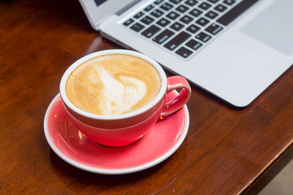 a cup of coffee on a saucer next to a laptop