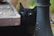 A playful black cat peeking out from behind a laptop on a wooden desk.