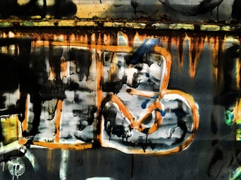Vibrant graffiti art with abstract shapes and drips of paint in shades of orange, black, and blue on a textured surface.