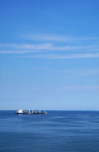 A vibrant photo of a cargo ship cutting through deep blue ocean waters under a clear sky.