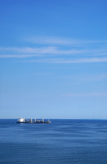 A vibrant photo of a cargo ship cutting through deep blue ocean waters under a clear sky.