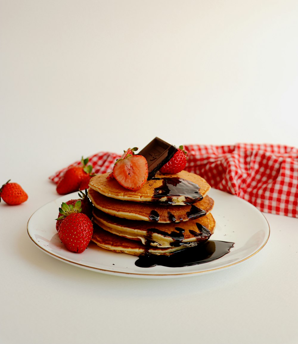 a white plate topped with pancakes covered in chocolate and strawberries