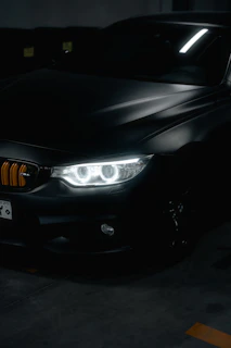 Close-up of a glossy black luxury car hood reflecting soft purple neon lights in a minimal modern garage.