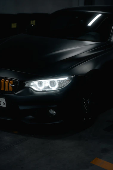 Close-up of a glossy black luxury car hood reflecting soft purple neon lights in a minimal modern garage.