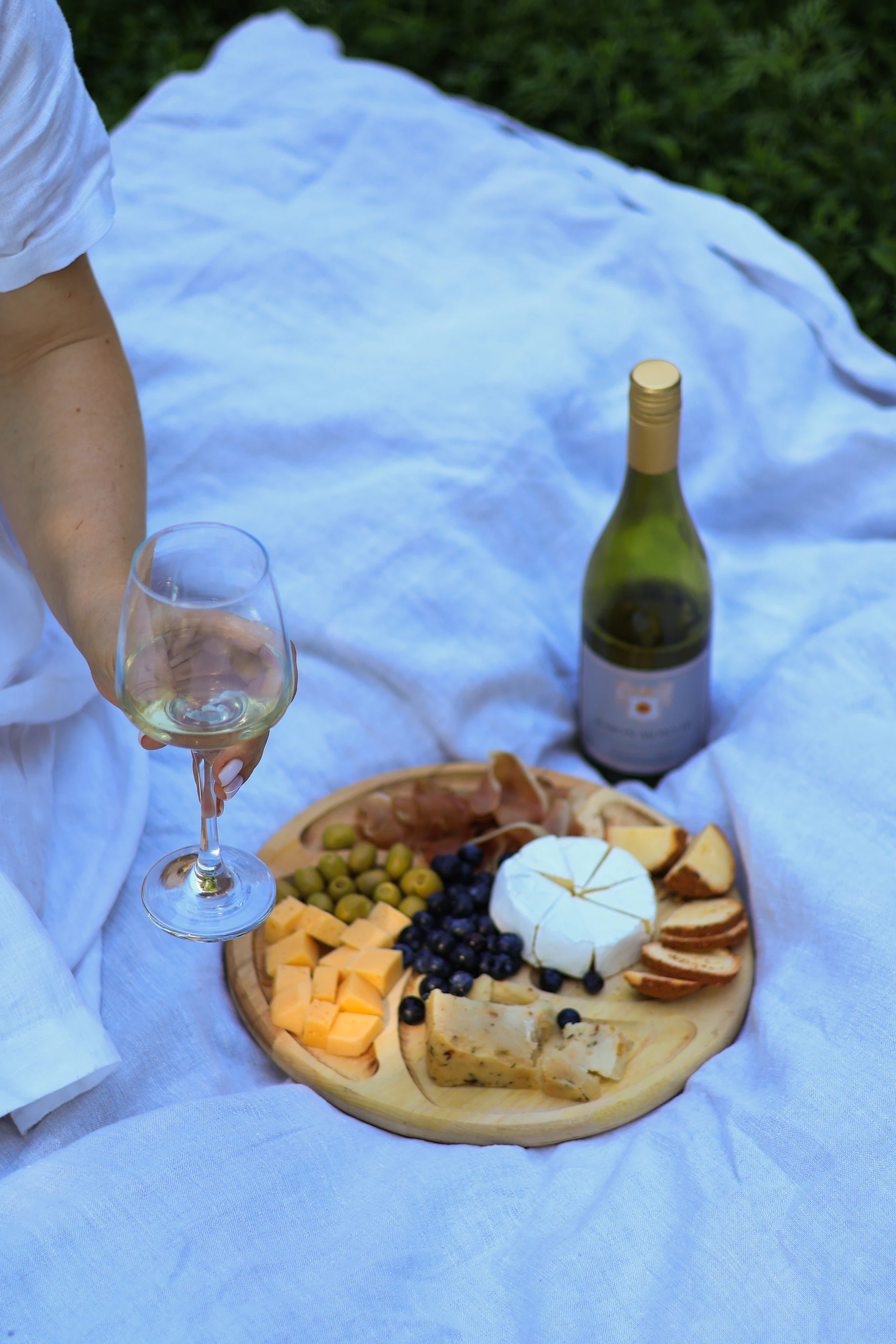 An overhead view of a scenic post-run picnic setup featuring various wine bottles, cheese, and fresh fruit laid out on a cozy blanket.