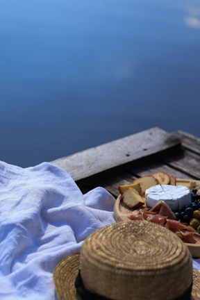 A smiling woman savoring a rustic cheese platter outdoors with a coastal view.