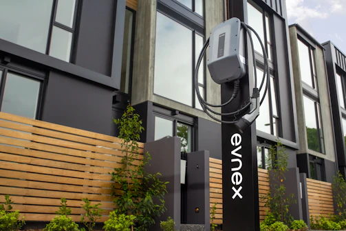 A modern electric vehicle charging at a stylish Totverde EV charger station surrounded by trees.