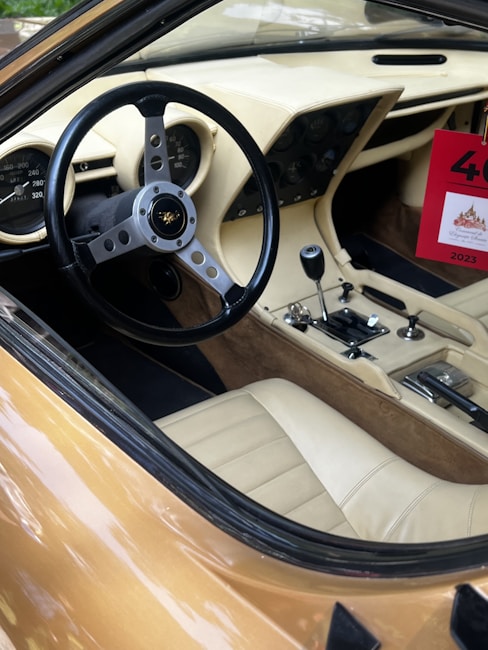 Interior of a vintage car showcasing a classic steering wheel with a logo, detailed dashboard with gauges, manual gear shift, and beige leather seats. A red sign with the number 40 and the year 2023 is visible hanging from the rear-view mirror.