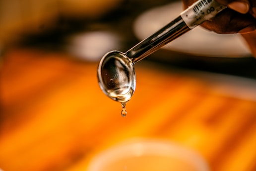 A close-up of golden syrup dripping from a spoon against a neutral background.
