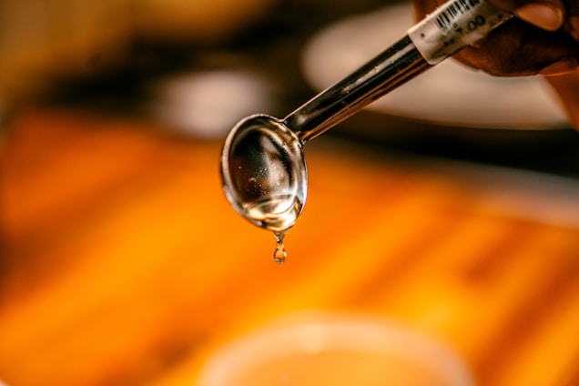 A close-up of golden maple syrup dripping from a wooden spoon against a rustic background.