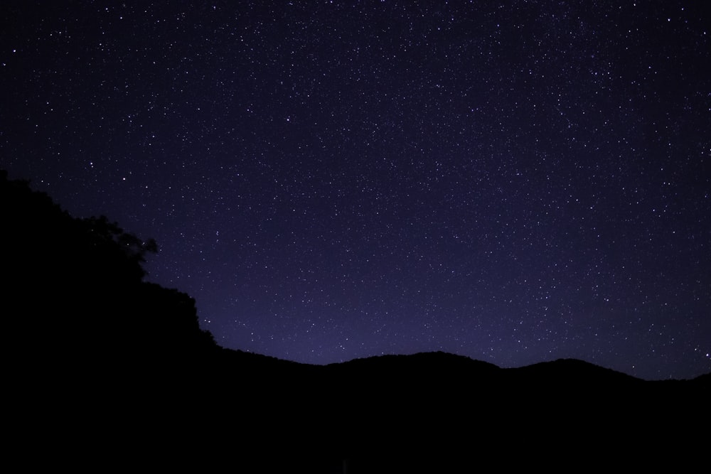 the night sky with stars above a mountain