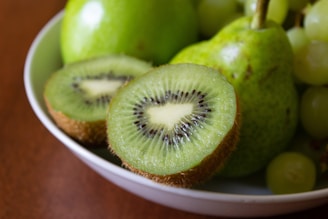 a white bowl filled with green fruit on top of a wooden table