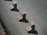 Three concrete barriers are aligned in a staggered pattern on a paved surface. Each barrier has a chunky, L-shaped design, casting shadows on the ground.