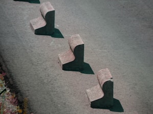 Three concrete barriers are aligned in a staggered pattern on a paved surface. Each barrier has a chunky, L-shaped design, casting shadows on the ground.