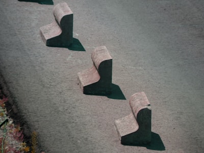 Three concrete barriers are aligned in a staggered pattern on a paved surface. Each barrier has a chunky, L-shaped design, casting shadows on the ground.