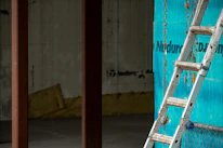 An industrial aluminium ladder positioned against a warehouse wall.