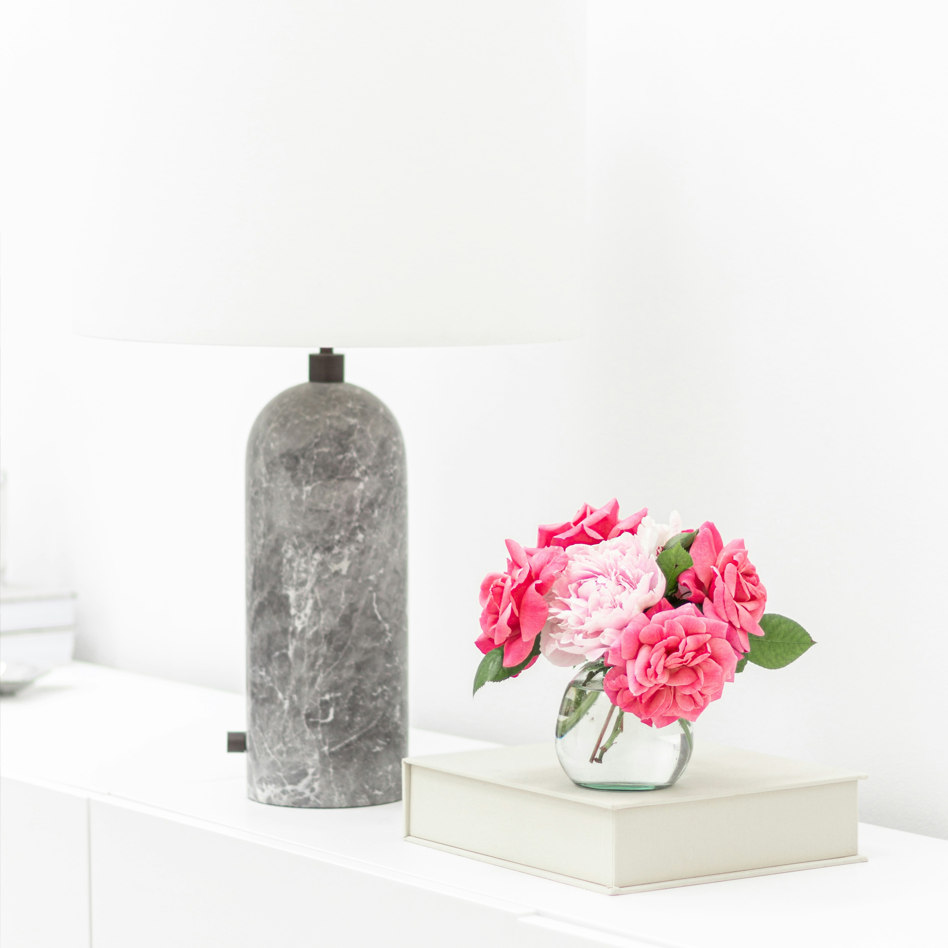 a vase with pink flowers on a white shelf