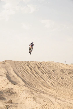 A dynamic motocross rider jumping over a dirt track with a sunset background.