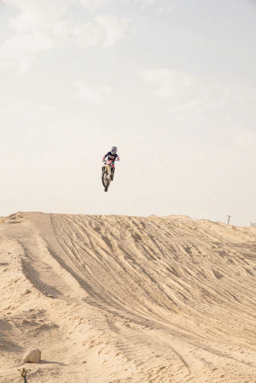A dynamic motocross rider jumping over a dirt track with a sunset background.