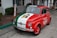 A small vintage car is parked on the street, featuring a tricolor paint job with green, white, and red, resembling the Italian flag. The hood displays an image, and the side is marked with a logo that includes the word 'AutoVino'.
