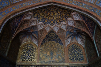 Artisan applying ornate stencil designs onto mosque ceiling panels.