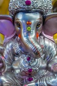 A detailed silver statue of an elephant-headed deity adorned with intricate jewelry and brightly colored embellishments.