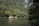 People wearing life jackets are paddling small boats on a calm river surrounded by lush greenery and tall cliffs. The scene conveys a sense of peace and adventure as they explore the serene natural environment.