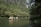 People wearing life jackets are paddling small boats on a calm river surrounded by lush greenery and tall cliffs. The scene conveys a sense of peace and adventure as they explore the serene natural environment.
