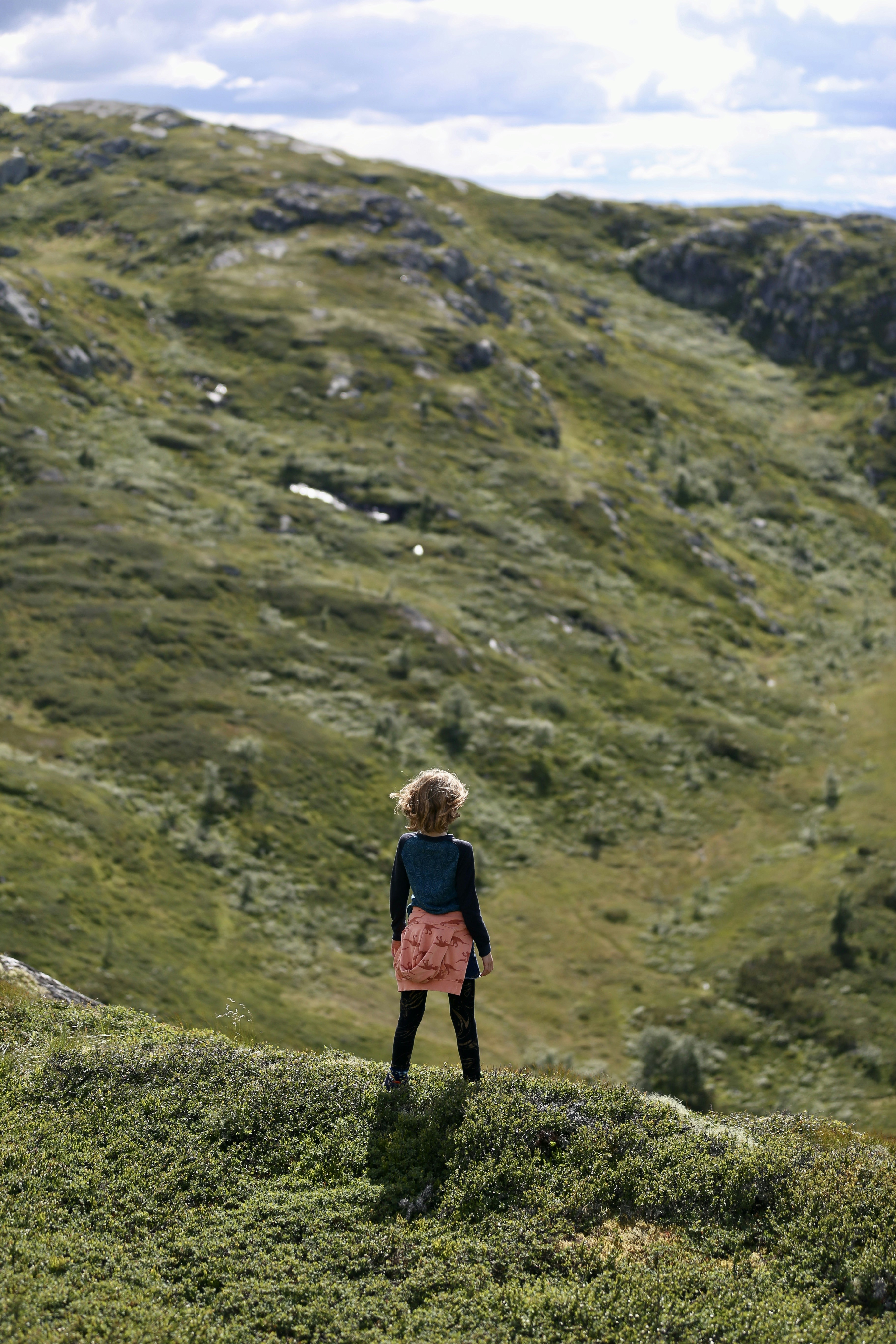 a little girl standing on top of a lush green hillside
