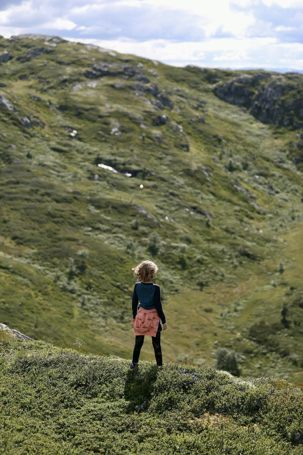 a little girl standing on top of a lush green hillside