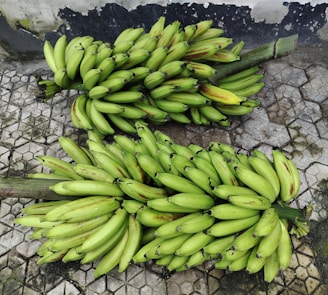 Several large clusters of green bananas are placed on a textured, patterned concrete surface. The bananas are fresh with slight imperfections visible near some tips.