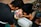 A group of individuals, including a child wearing a cap with a colorful design, are practicing CPR on a dummy. The scene appears to take place outdoors on a textured black mat. The participants are focused on their task, with one child leaning in, presumably to perform mouth-to-mouth resuscitation.