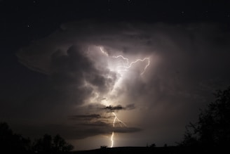 A dramatic shot of a swirling tornado under a dark, stormy sky with lightning illuminating the scene.