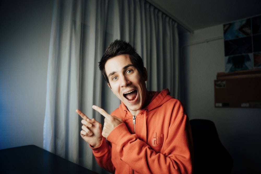 a man in an orange hoodie making a peace sign
