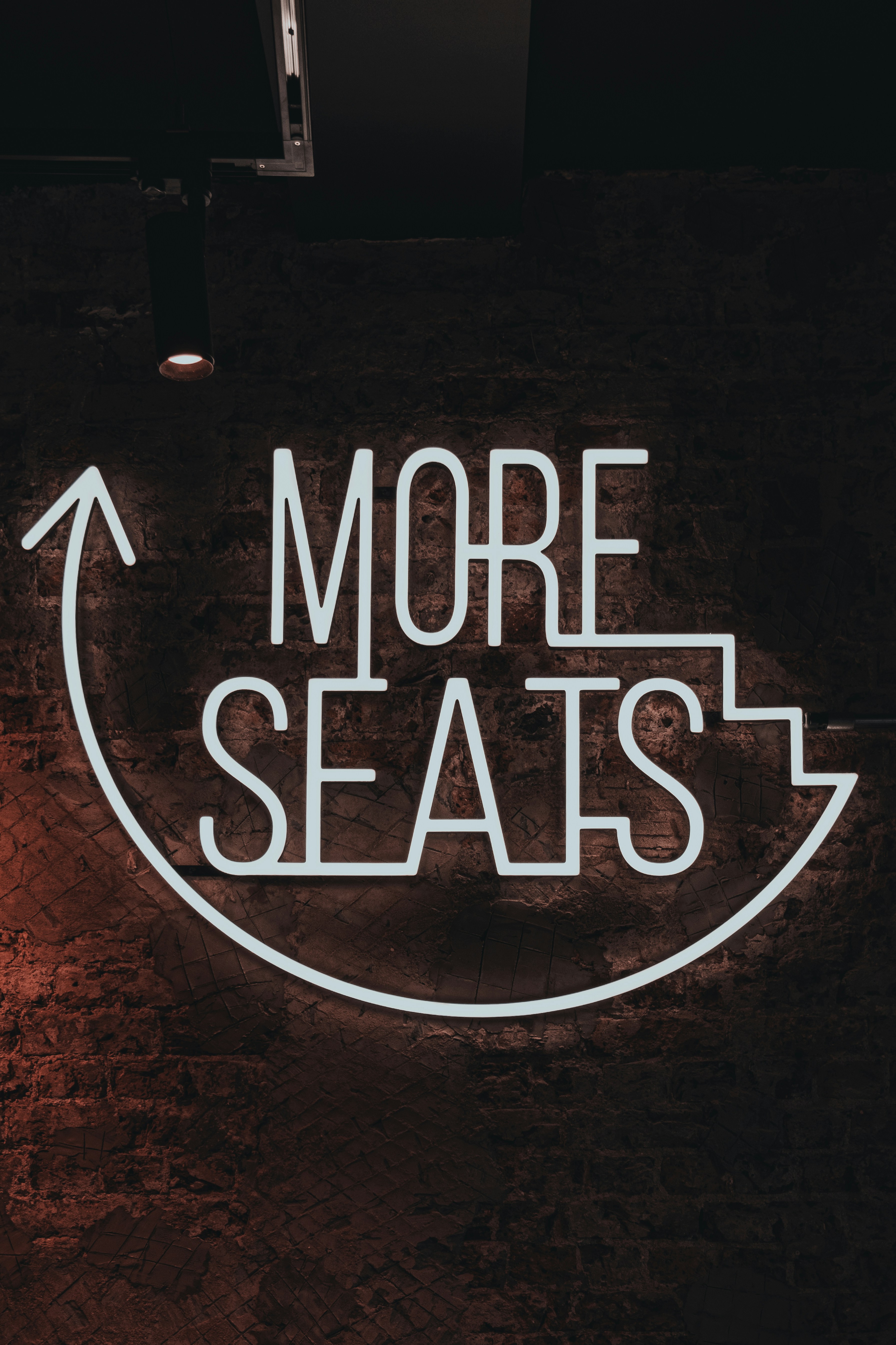 a neon sign that says more seats on a brick wall