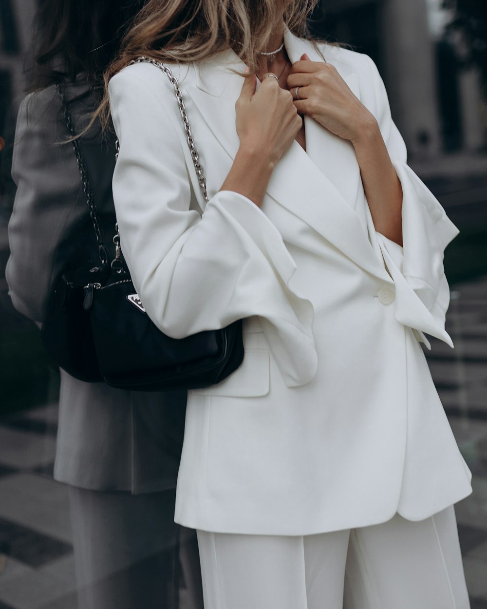 a woman wearing a white suit and holding a black purse