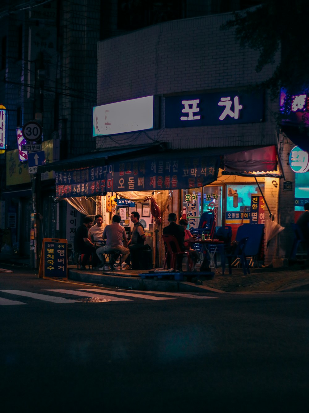 a group of people sitting outside of a restaurant at night