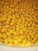 A collection of numerous yellow plastic heads with various facial expressions, resembling LEGO character heads, piled together in a large container.