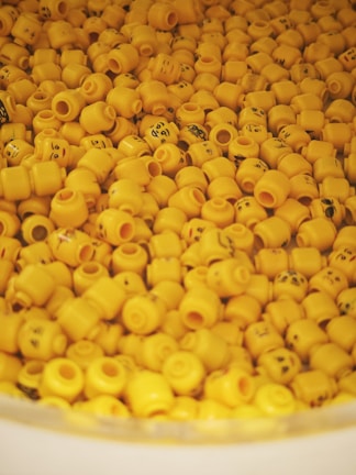 A collection of numerous yellow plastic heads with various facial expressions, resembling LEGO character heads, piled together in a large container.