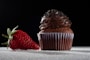 a chocolate cupcake and a strawberry on a table