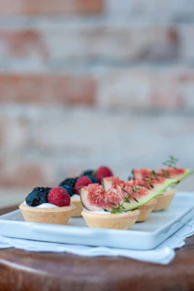 An assortment of mini tartlets with various fruit toppings displayed on a vintage ceramic plate.