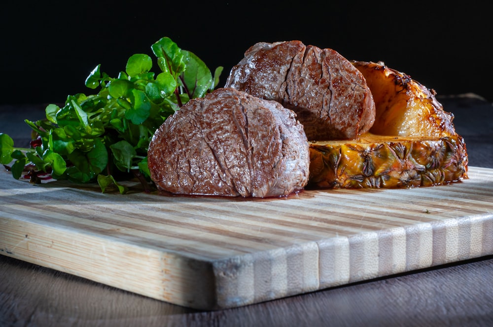 a wooden cutting board topped with meat and vegetables