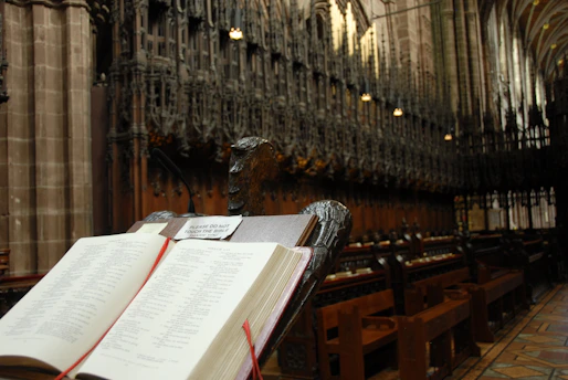 Open Bible resting on a wooden lectern with soft natural light highlighting the text.