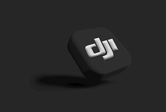 A three-dimensional black cube with the letters 'dji' prominently embossed in white on one side. The cube casts a subtle shadow against a dark gray background, giving a sleek and modern aesthetic.